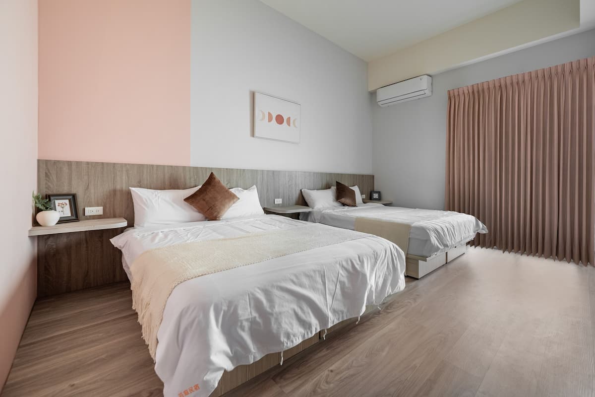 A hotel room with two beds, a wooden headboard, a bedside table with a plant, a framed picture, and a large window with curtains.