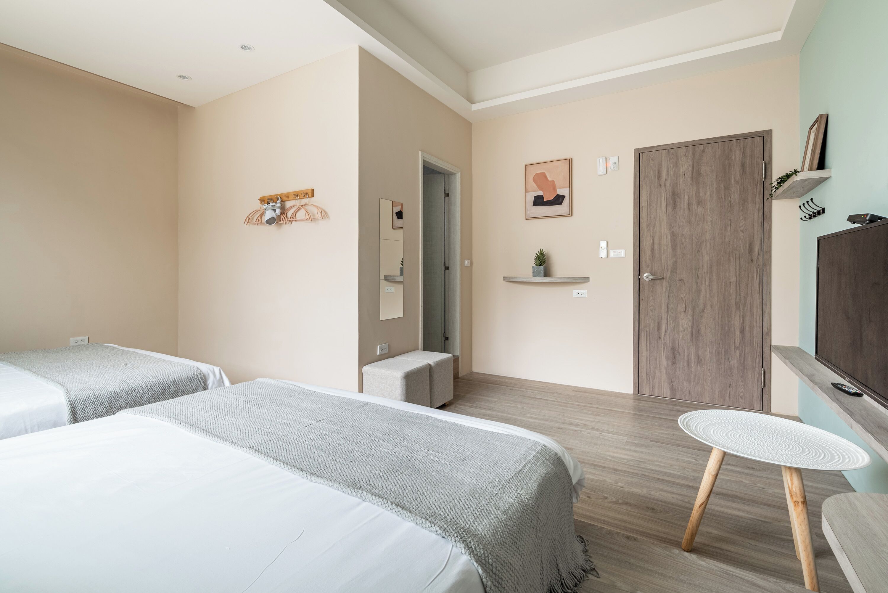 A hotel room with two beds, a small round table, a TV, a wooden door, and a mirror.