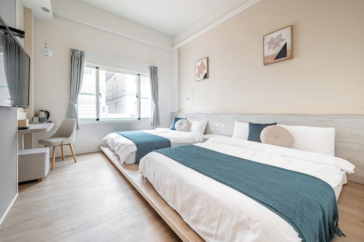 A modern hotel room with two beds, a desk, and a chair.