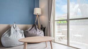 A room with a round wooden table, two bean bags, a floor lamp, and a view of outdoor furniture through a large window. - Penghu Yun Ting Style Inn (Magong)