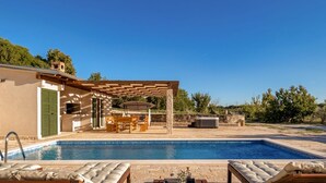 A swimming pool with lounge chairs, a covered patio with outdoor furniture, and a stone wall in the background. - Villa Oliveto with pool,jacuzzi & sauna (Donji Kašic)