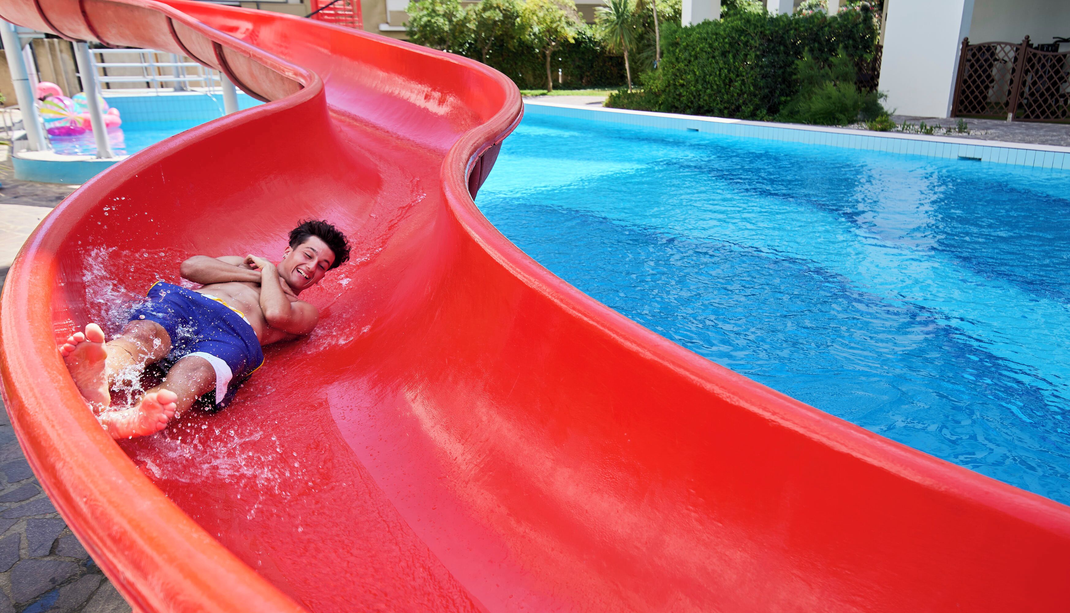 A person sliding down a red water slide into a pool.