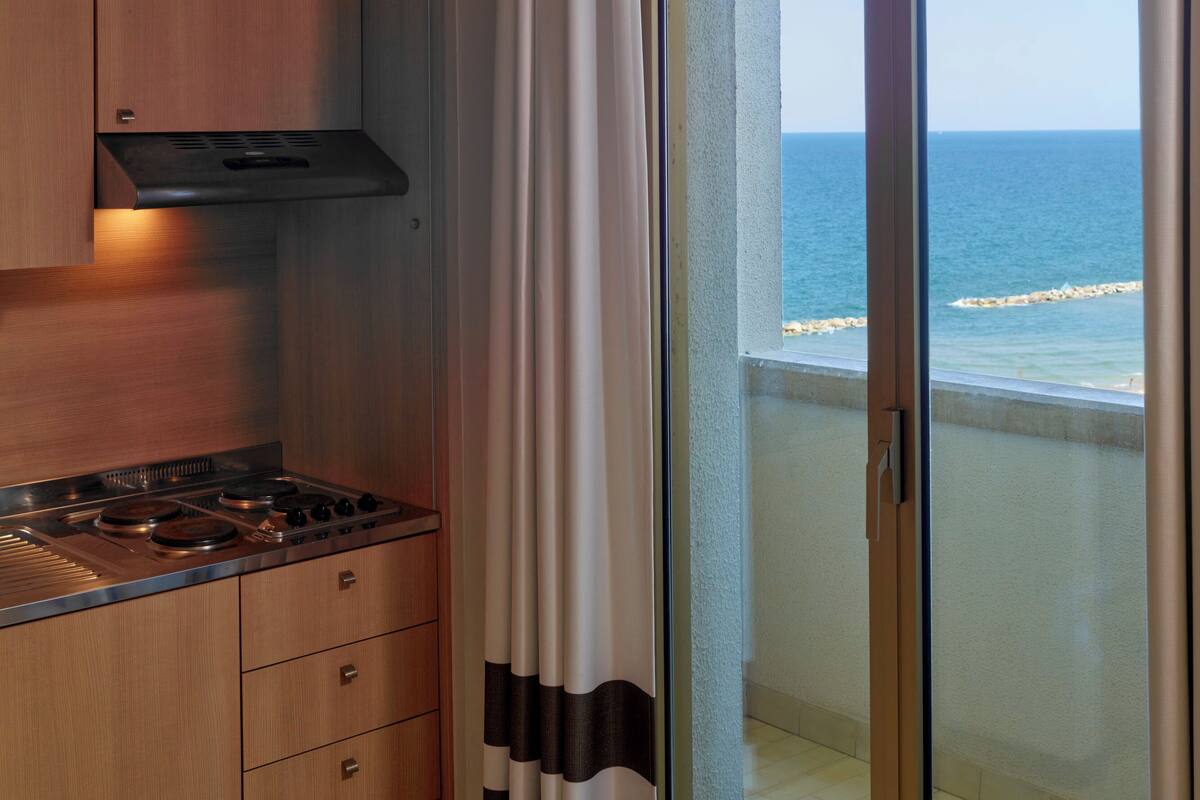 Une cuisine moderne équipée d’une cuisinière, de placards et offrant une vue sur l’océan grâce à une porte-fenêtre coulissante.