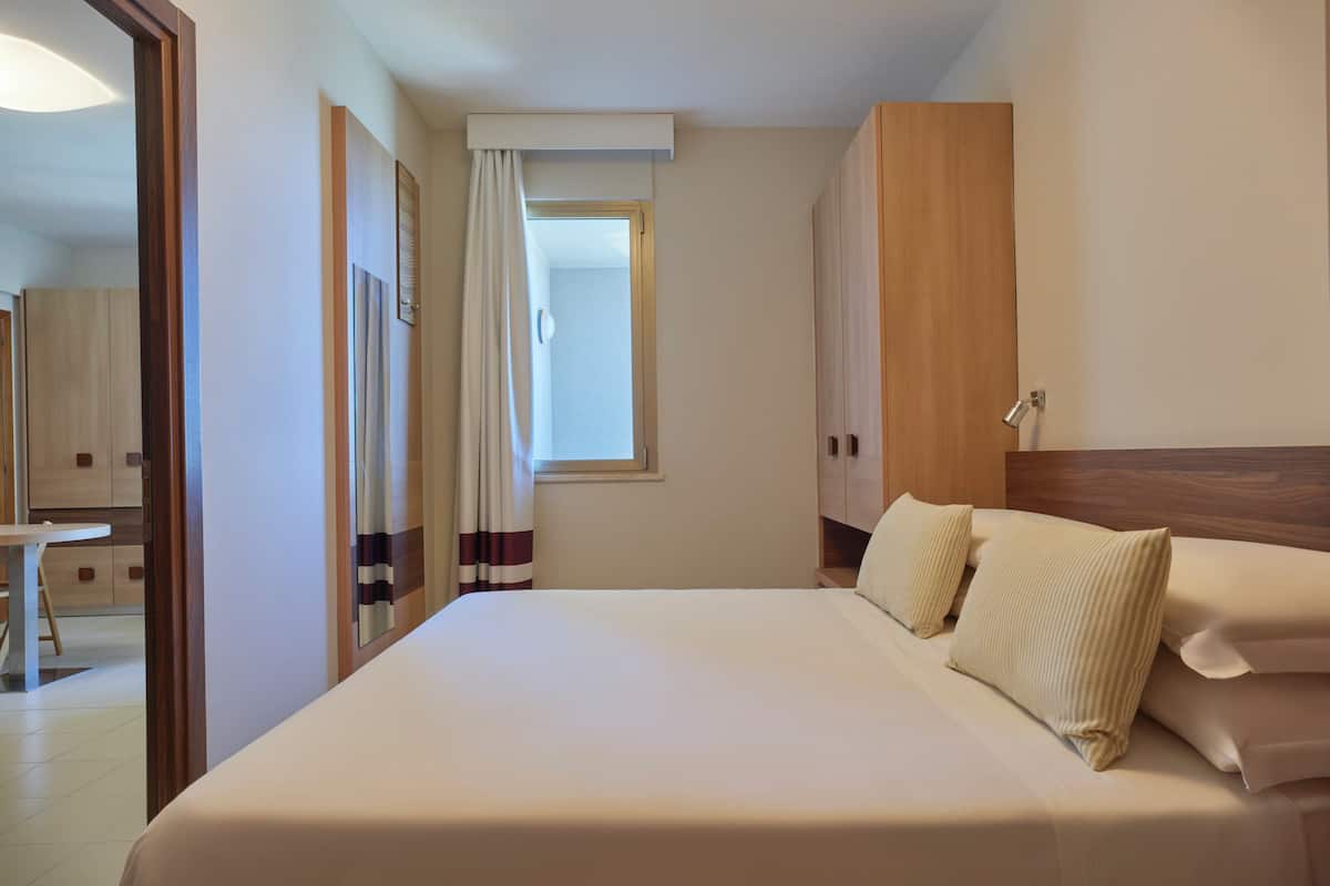 Une chambre d’hôtel avec un grand lit, une armoire en bois et une fenêtre avec des rideaux.