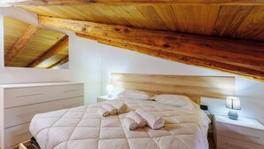 Une chambre avec un plafond en bois, un lit doté d’un matelas matelassé, deux tables de chevet avec des lampes et une petite table de nuit avec une lampe.