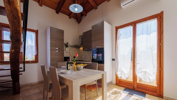 Une cuisine moderne avec des meubles en bois, une table à manger avec des chaises et une grande porte-fenêtre coulissante donnant sur un balcon.