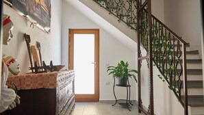 Un escalier orné d’une rampe en fer forgé, une porte en bois en bas et une plante en pot posée sur un petit piédestal.
