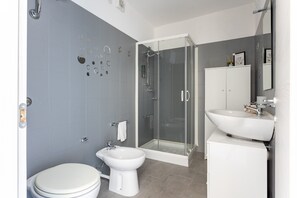 A modern bathroom with a toilet, bidet, glass-enclosed shower, and a sink with a cabinet.