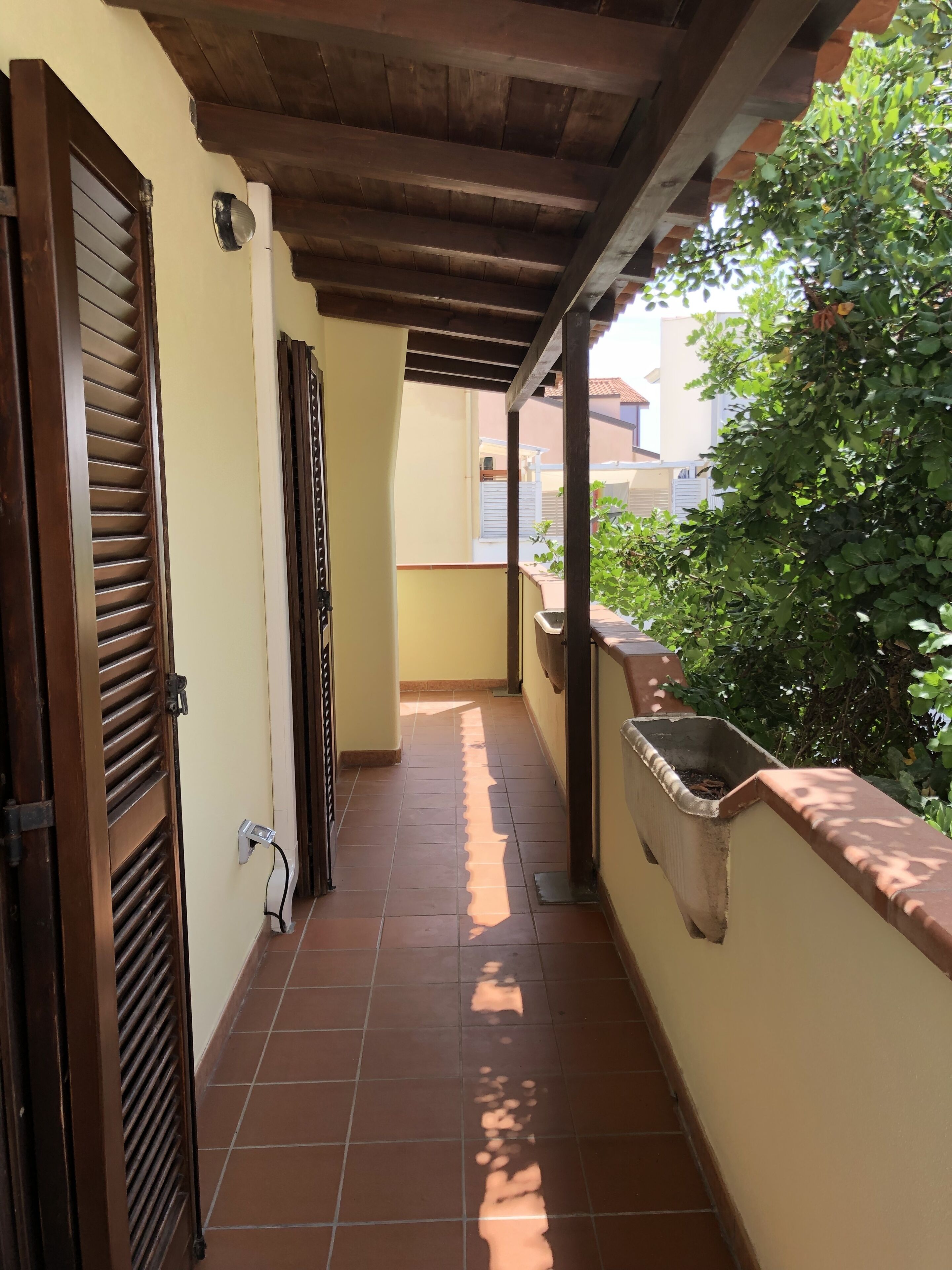 A covered corridor with tiled flooring, a wooden door, and a planter box.