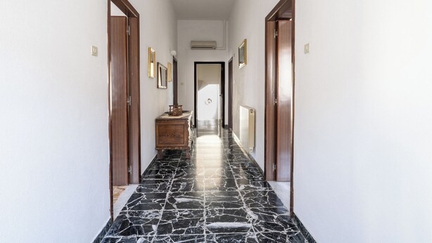 Un pasillo con suelo de mármol, puertas de madera y cuadros enmarcados en las paredes.