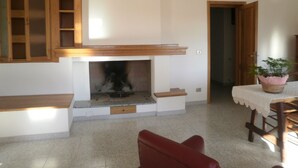 Una stanza con camino, mobili in legno, un tavolo da pranzo con una pianta e una sedia rossa.