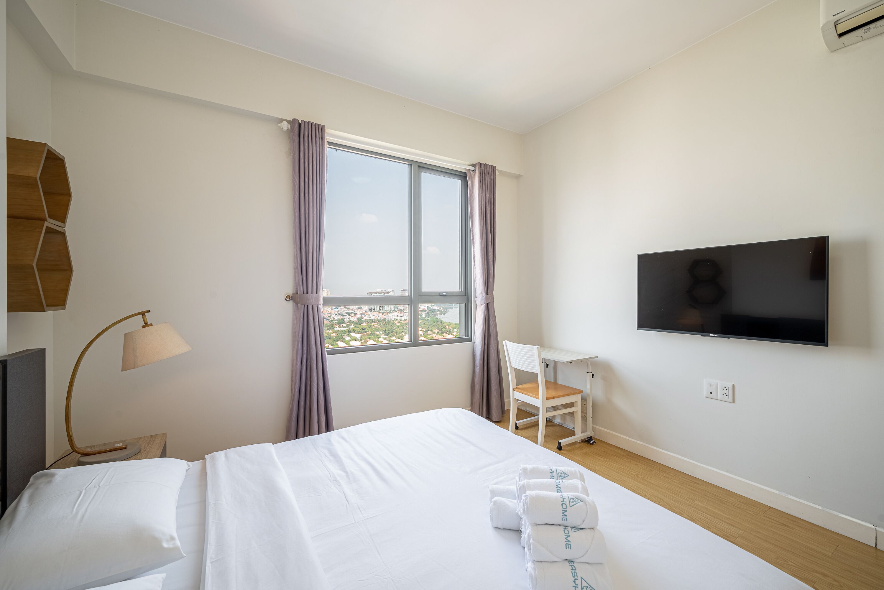 Habitación de hotel con cama, escritorio, silla, televisor y ventana con cortinas.