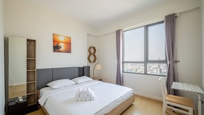 Ein Hotelzimmer mit Bett, Schreibtisch, Stuhl, Fenster mit Stadtblick, einem Gemälde und einem Holzschrank.