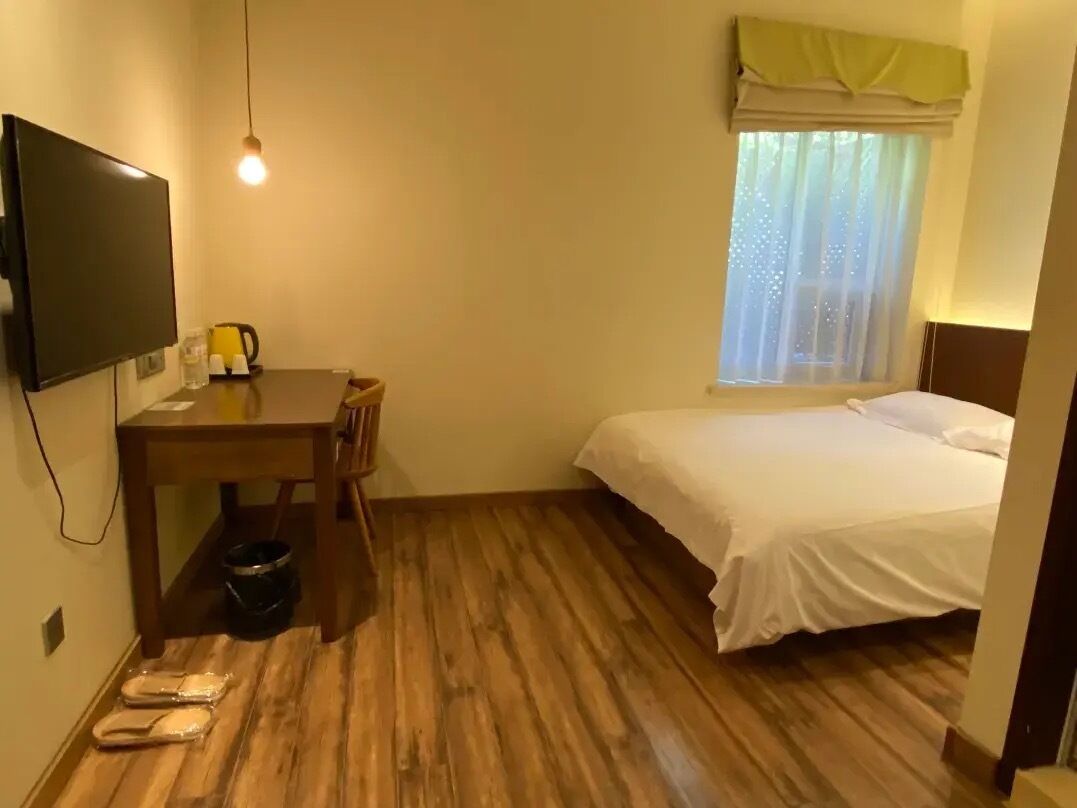 A small room with a bed, a desk with a chair, a television, and a window with curtains.