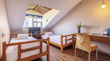 Une chambre avec deux lits superposés en bois, un bureau avec une chaise et une fenêtre donnant sur un immeuble.