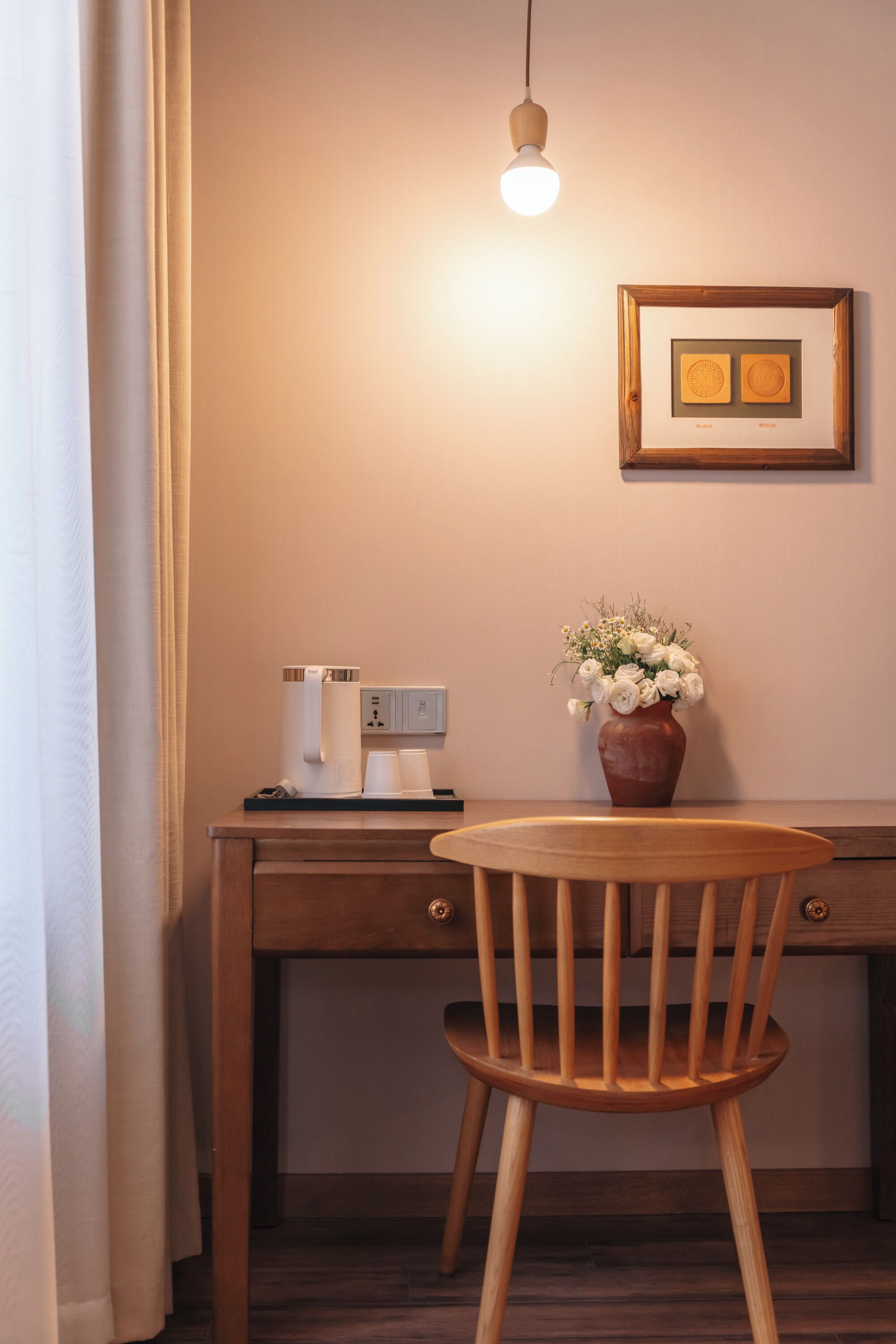 A wooden desk with a coffee machine, a vase with flowers, and a framed picture on the wall.