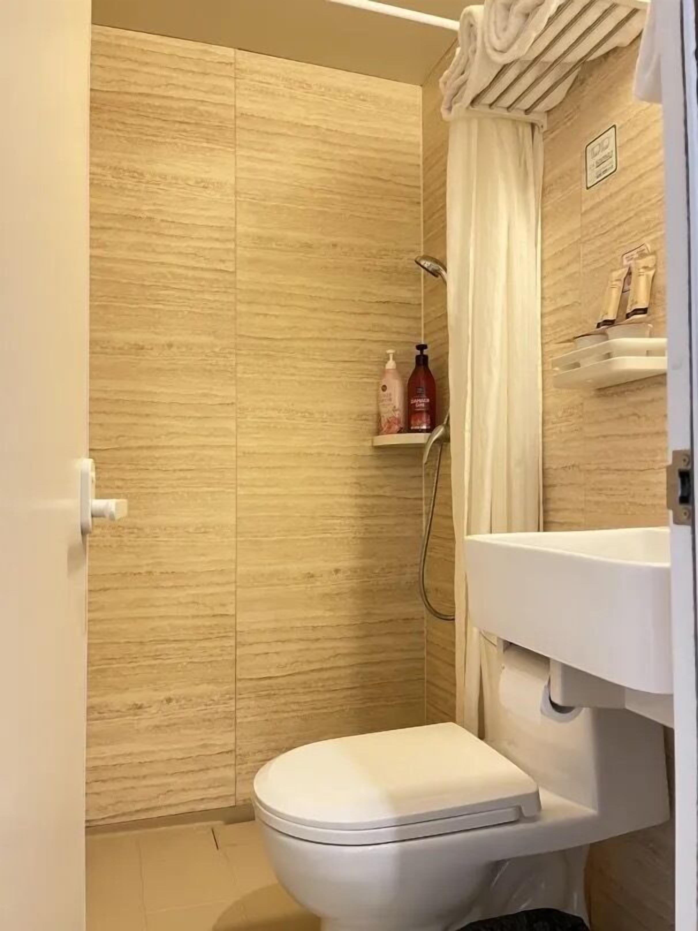 A bathroom with a shower, toilet, and a shelf with toiletries.