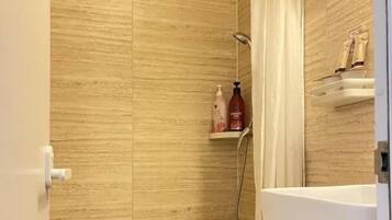 A bathroom with a shower, toilet, and a shelf with toiletries.