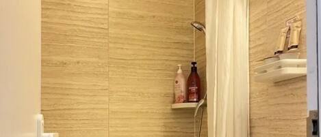 A bathroom with a shower, toilet, and a shelf with toiletries.