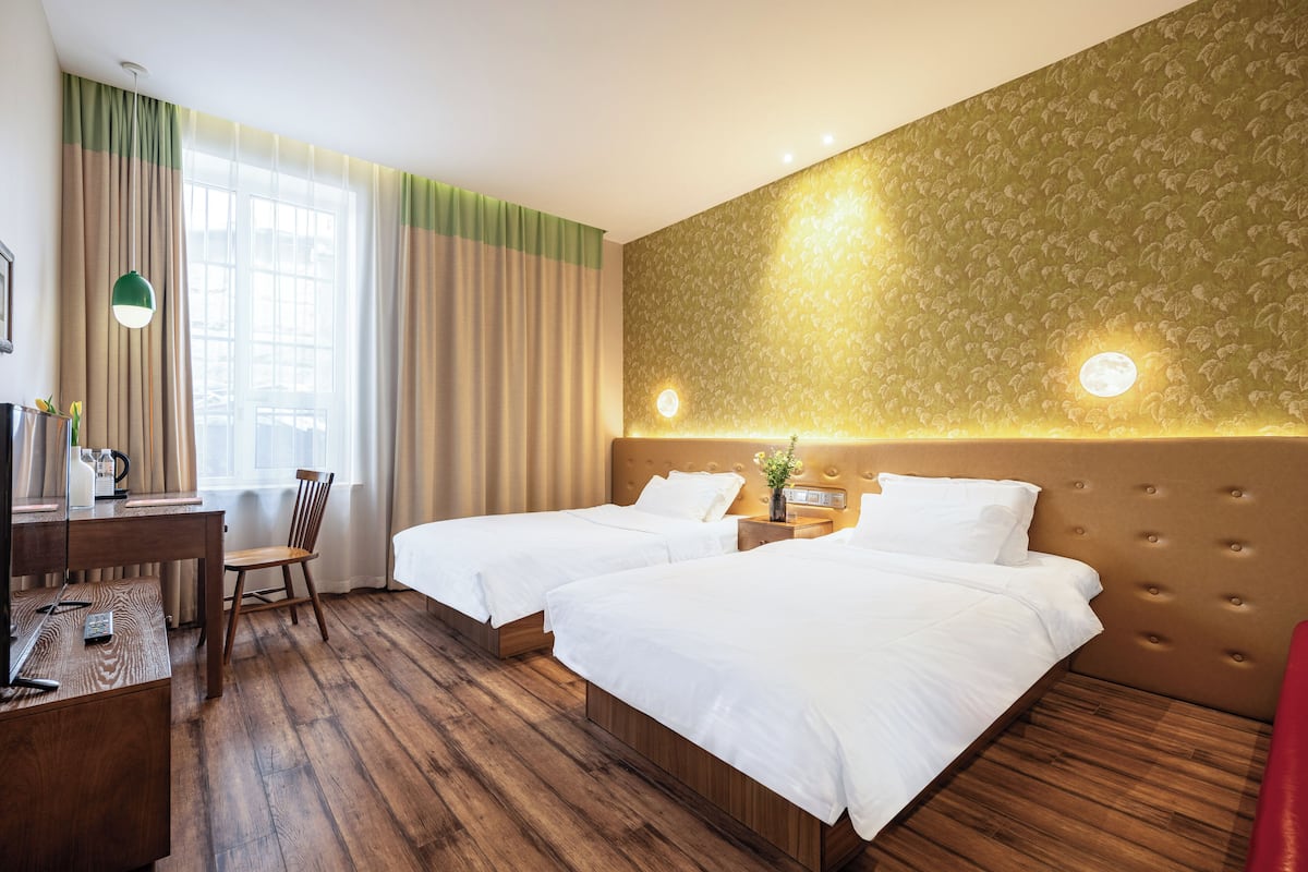 A hotel room with two beds, a desk, a chair, and a large window with curtains.