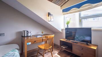 A bedroom with a bed, a desk with a chair, a TV, and a window with a view of buildings.