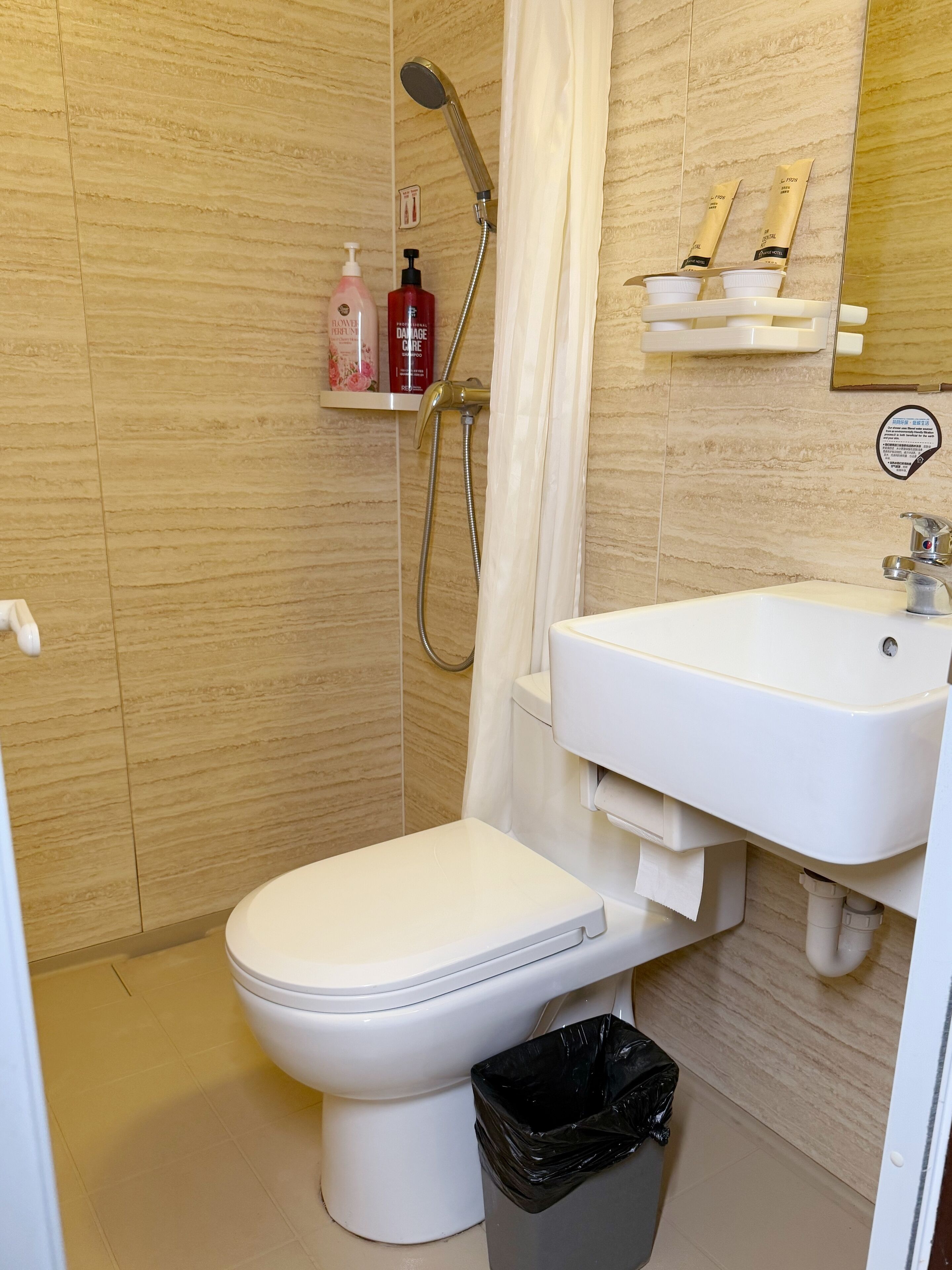 A modern bathroom with a toilet, shower, sink, and a trash bin.