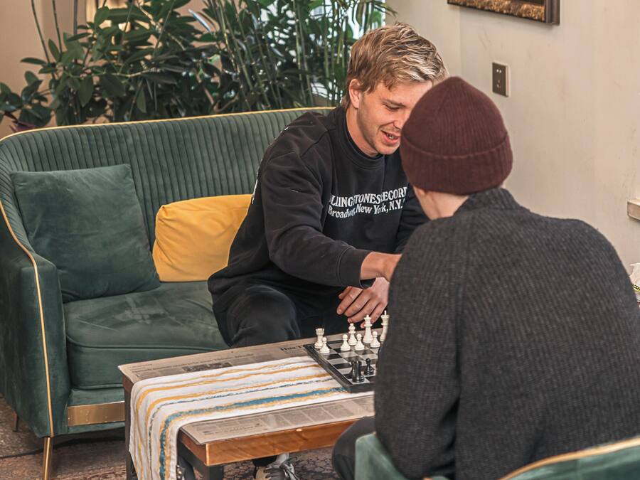 A room with a green sofa, a chess table, and a lamp.