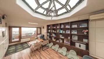 A room with a skylight, wooden flooring, a desk with chairs, a bookshelf, and a view through a door.