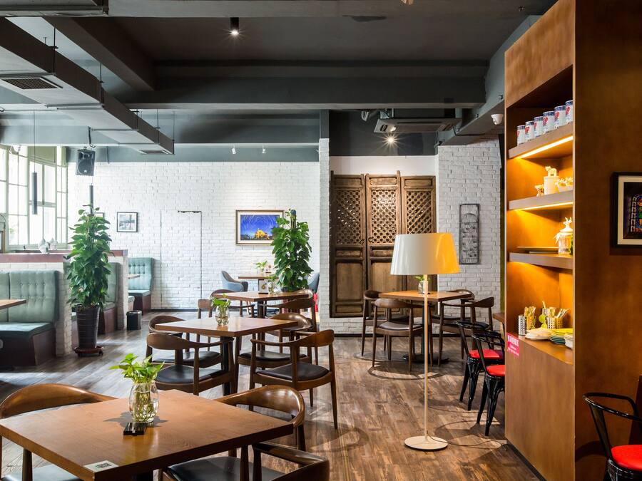 Um restaurante com mesas e cadeiras de madeira, um espaço de bar e uma parede de tijolos com janela.