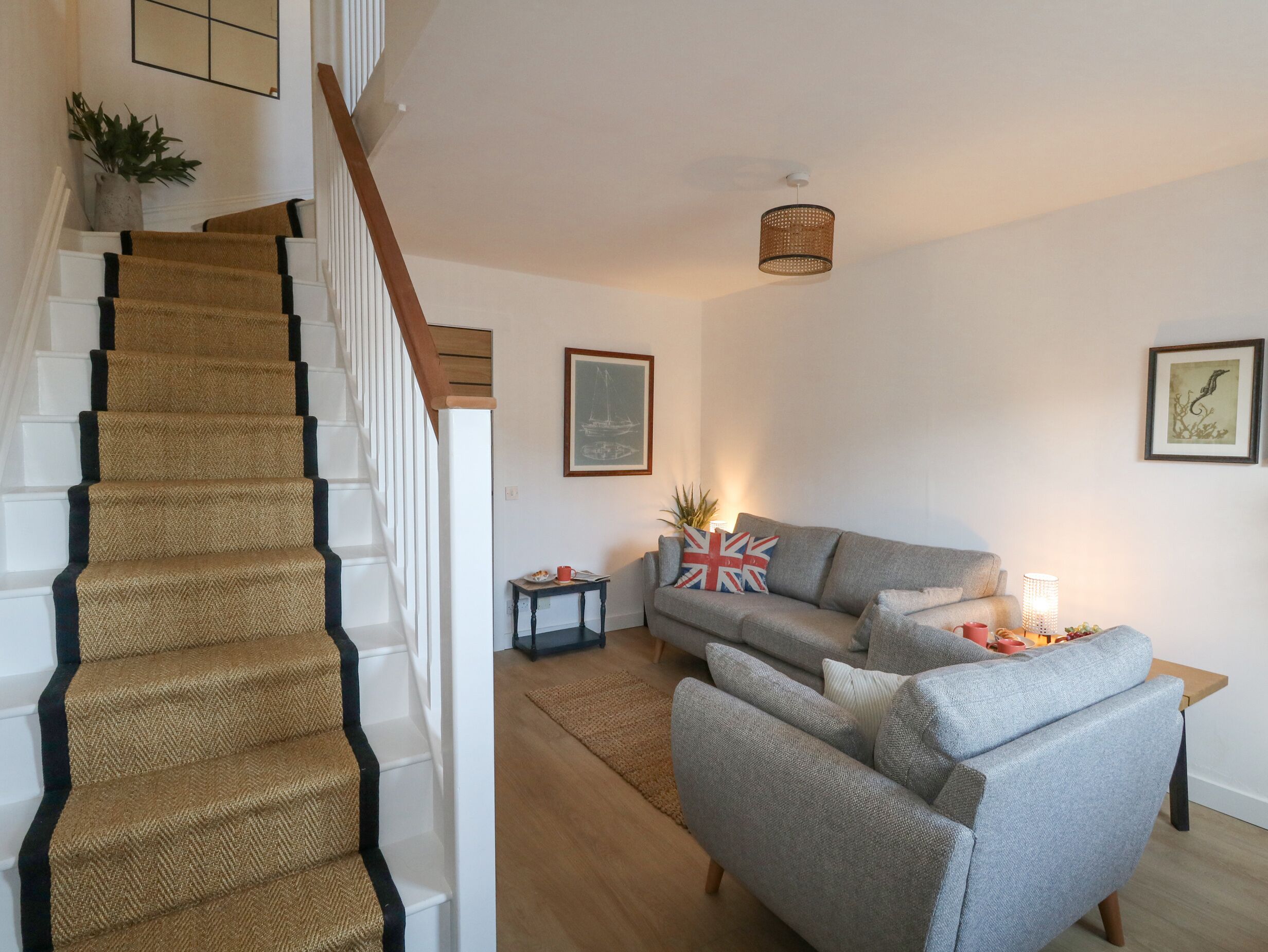 A staircase with a textured carpet, a grey sofa set, a small table with a lamp, and a framed picture on the wall.