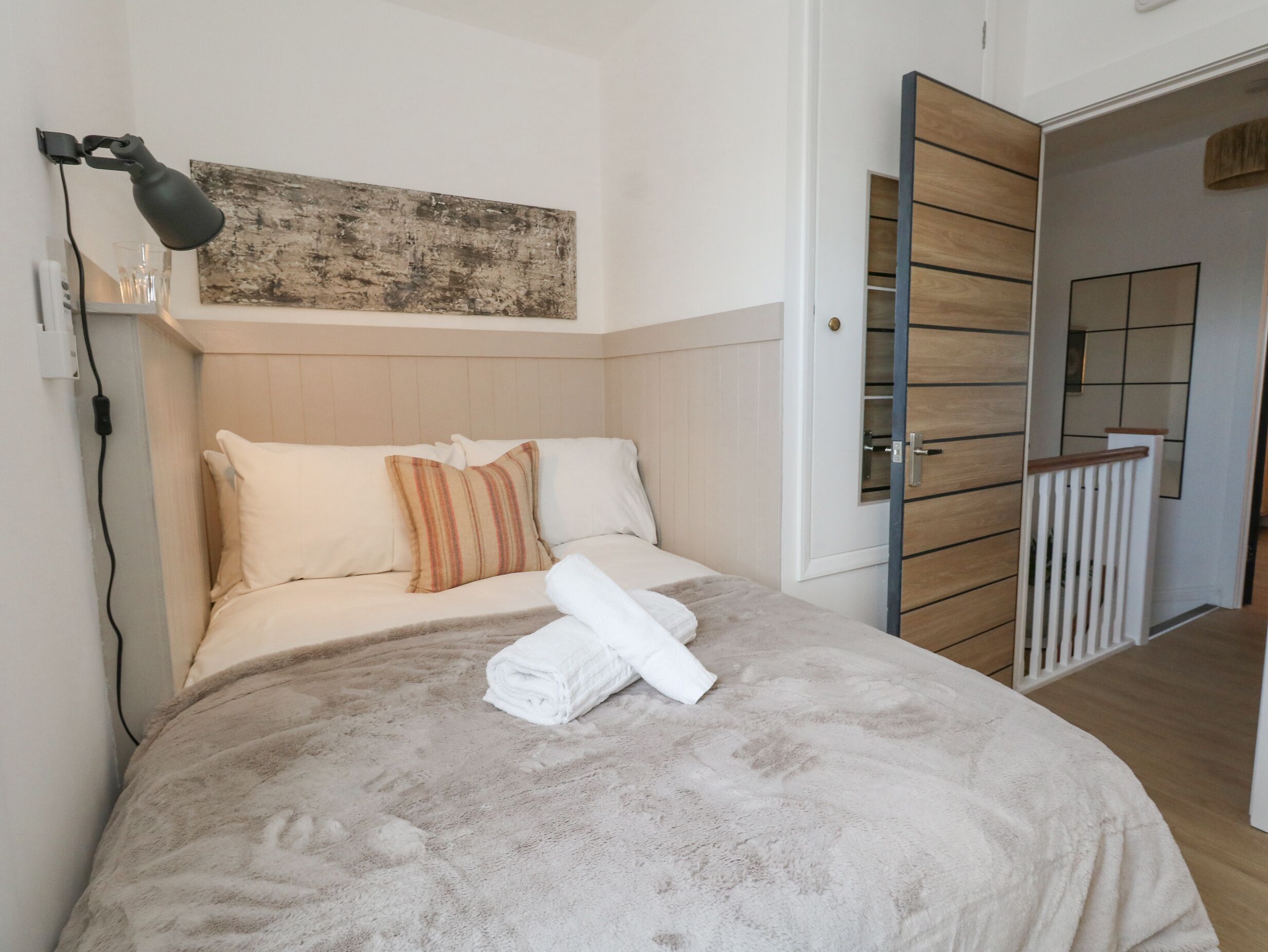 A neatly made bed with a folded towel, a lamp, and a wooden headboard.