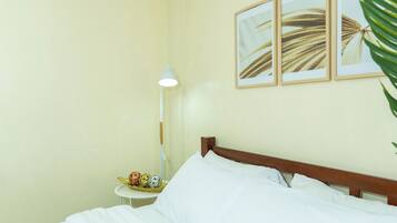 A neatly made bed with white linens, a bedside lamp, and a small table with decorative items.