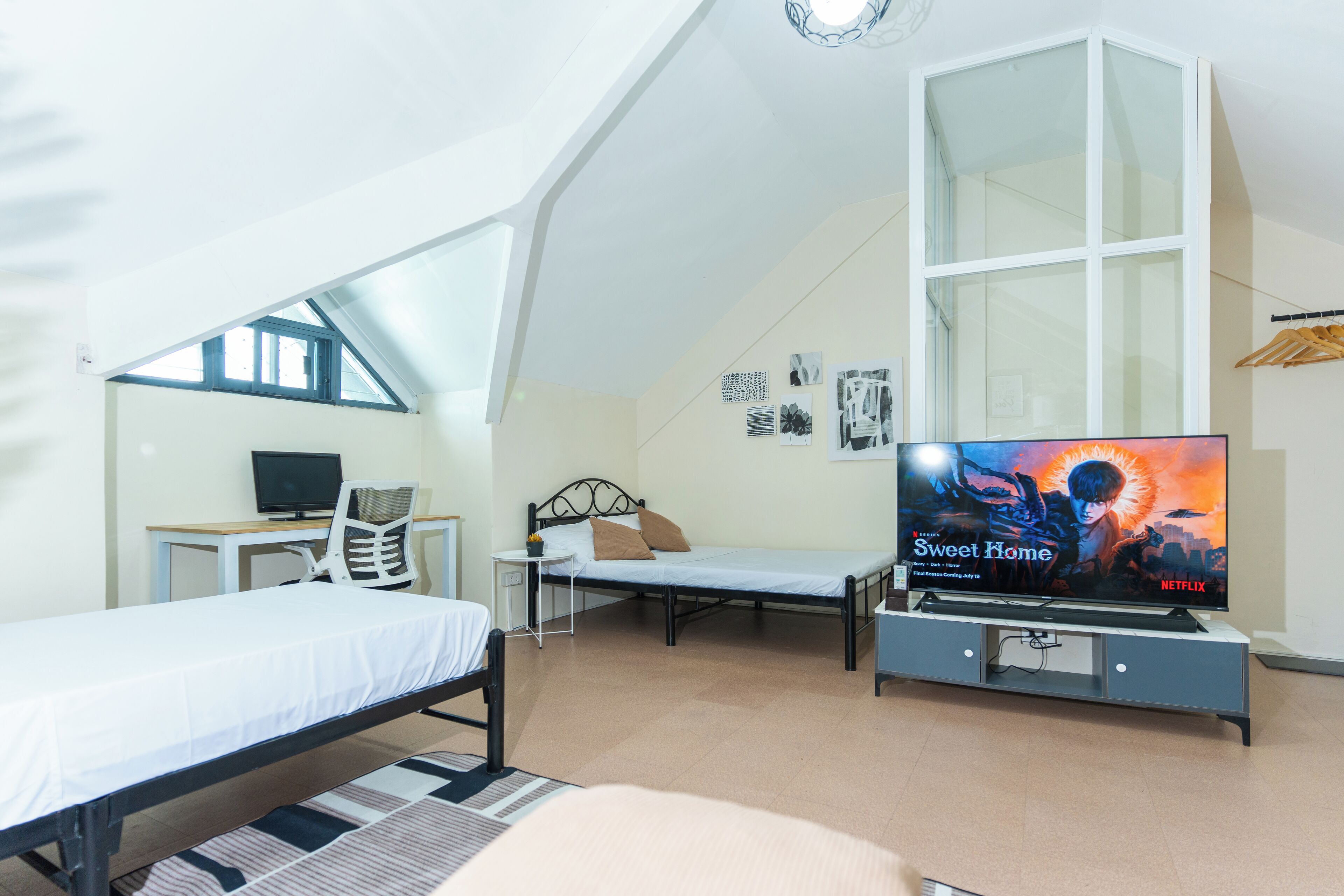 A bedroom with a bed, a desk with a computer, a TV, and a window.