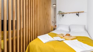Een keurig opgemaakt slaapkamer met een bed, een nachtkastje, een plank met planten en een houten roomdivider.