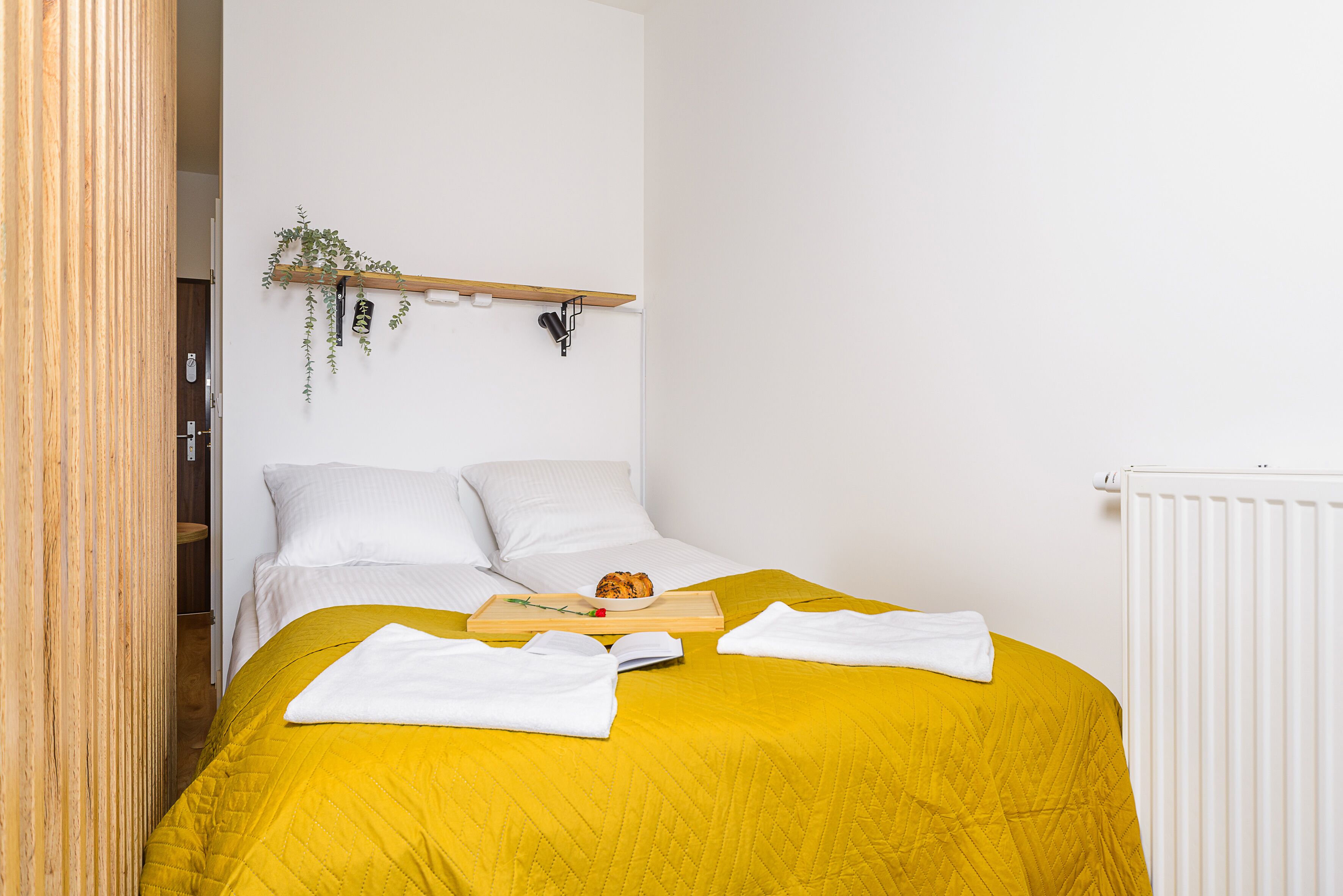 A bed with a yellow bedspread, white pillows, and a tray with a croissant and a book.