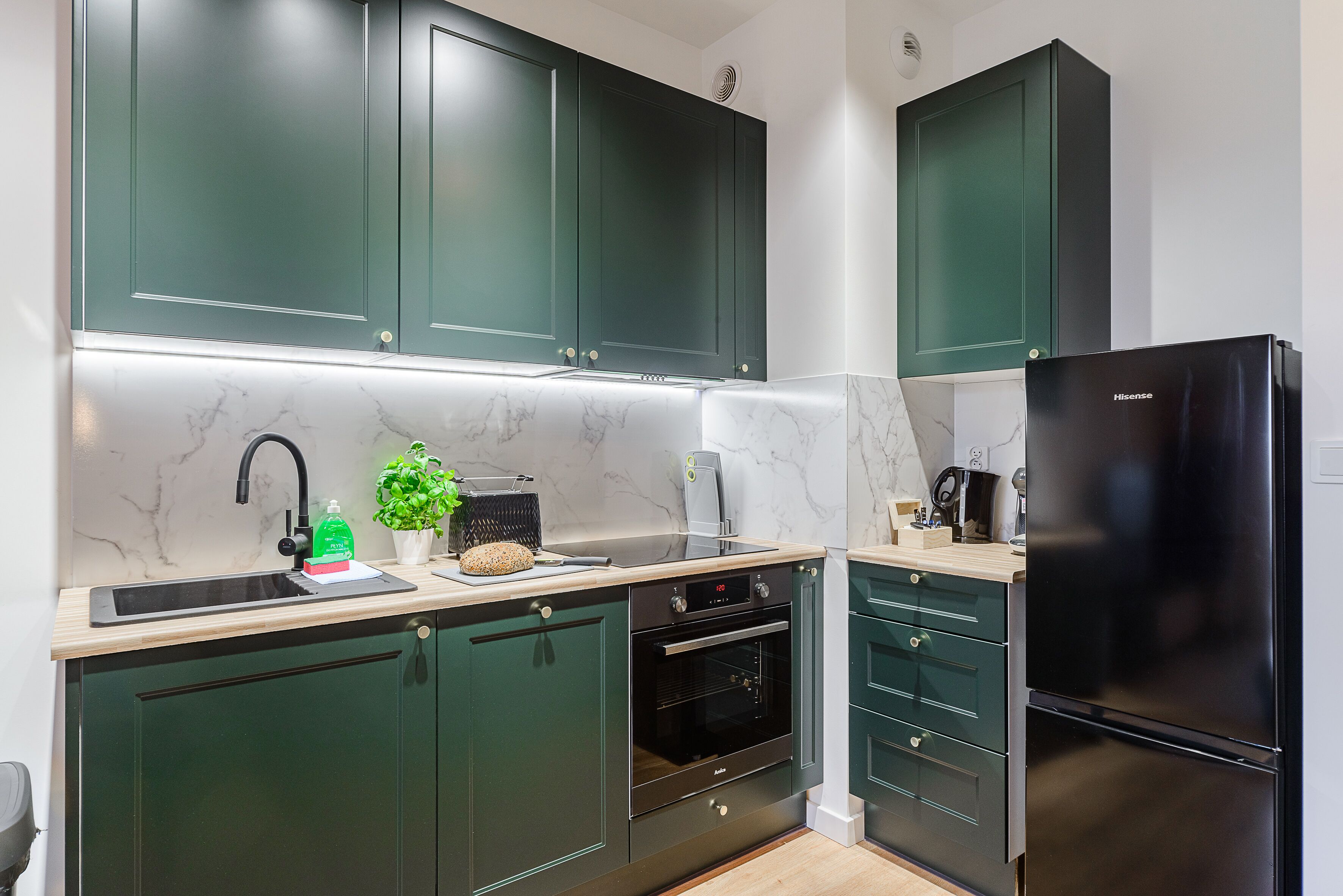 A modern kitchen with dark green cabinets, a black refrigerator, a built-in oven, and a marble backsplash.