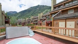 A hot tub area with a wooden deck and a mountain backdrop. - Horsethief Ski In Out Studio / Fireplace / Hot tub (Panorama)