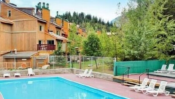 A swimming pool with lounge chairs, a wooden building, and a forested hillside in the background. - Horsethief Ski In Out Studio / Fireplace / Hot tub (Panorama)