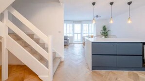 A modern kitchen with a central island, white staircase, and pendant lighting. - Modern Apartment in Paddington (Greater London)