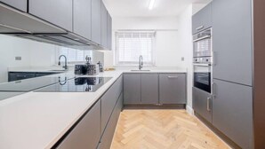 A modern kitchen with grey cabinets, a white countertop, and a herringbone wood floor. - Modern Apartment in Paddington (Greater London)