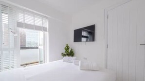 A bedroom with a large bed, a TV mounted on the wall, and a balcony with a view of the city. - Modern Apartment in Paddington (Greater London)