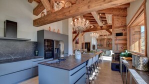 Une cuisine spacieuse dotée d’un grand îlot central, de poutres en bois et d’un lustre.