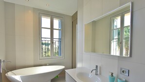 A modern bathroom with a freestanding bathtub, a large mirror, and a white vanity with two blue cups.