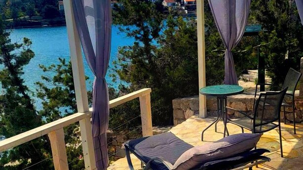 A terrace with two sun loungers, a table, and chairs. The terrace overlooks a body of water and a hillside with houses. - Oliven Penthouse (Sutivan)