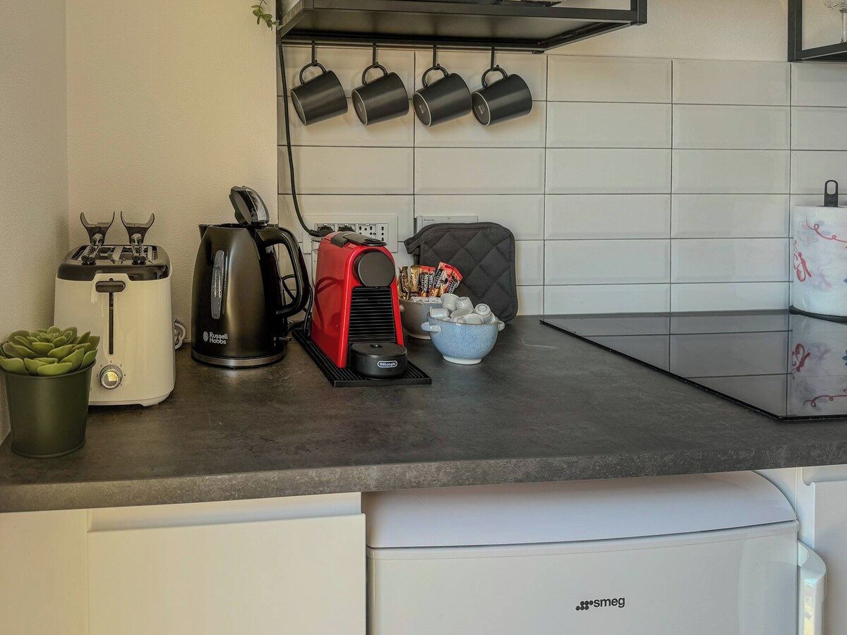 Une cuisine équipée d’un grille-pain, d’une cafetière rouge, d’une bouilloire et d’un bol à sucre posé sur le comptoir.