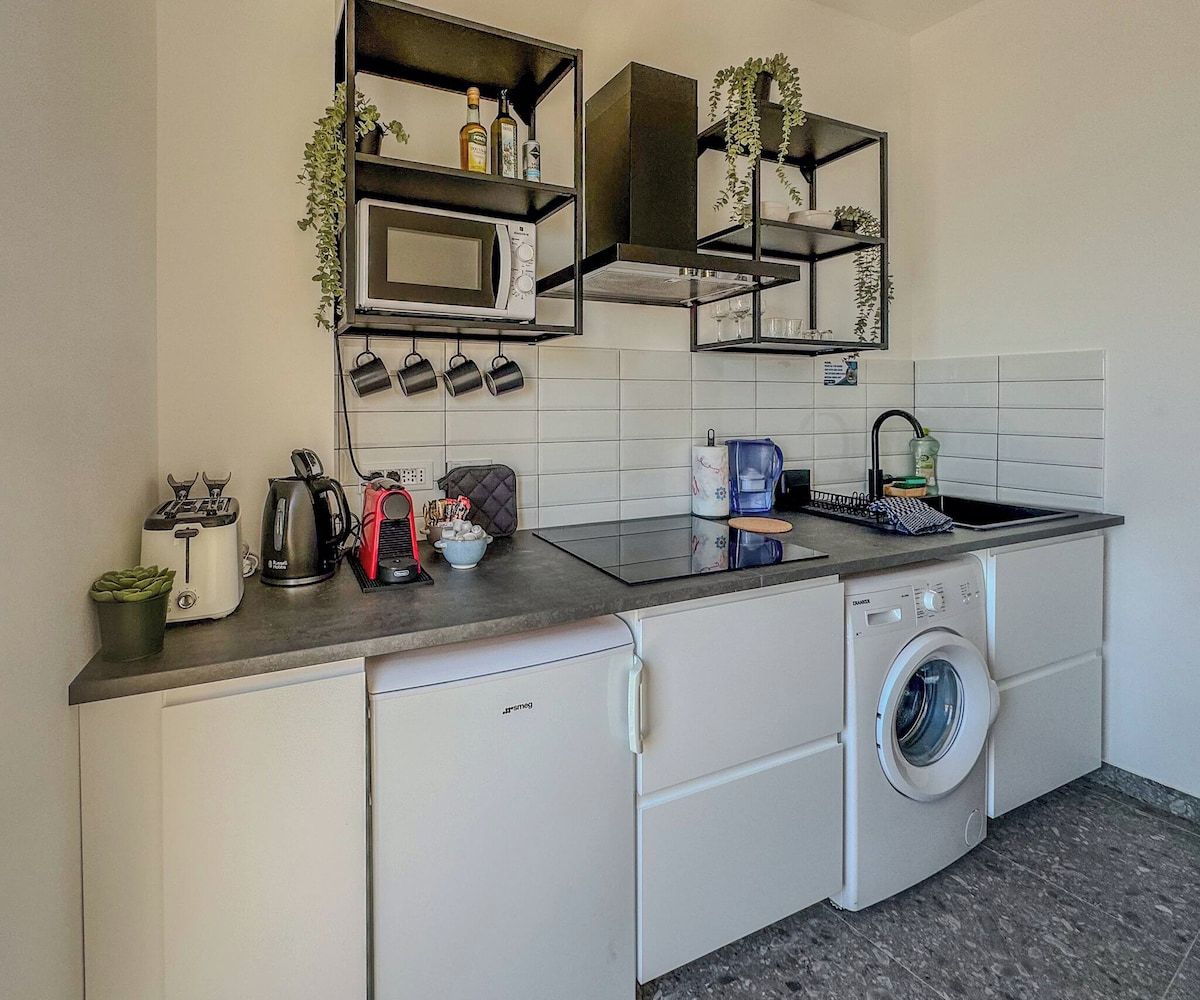 Eine kompakte Küche mit integriertem Mikrowellenherd, einer Kaffeemaschine, einem Toaster und einer Waschmaschine.