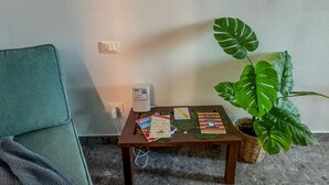 Una pequeña mesa de madera con libros y un dispositivo blanco, una silla verde y una planta grande de color verde.