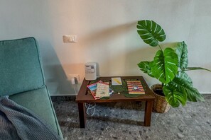 A small wooden table with books and a white device, a green chair, and a large green plant.