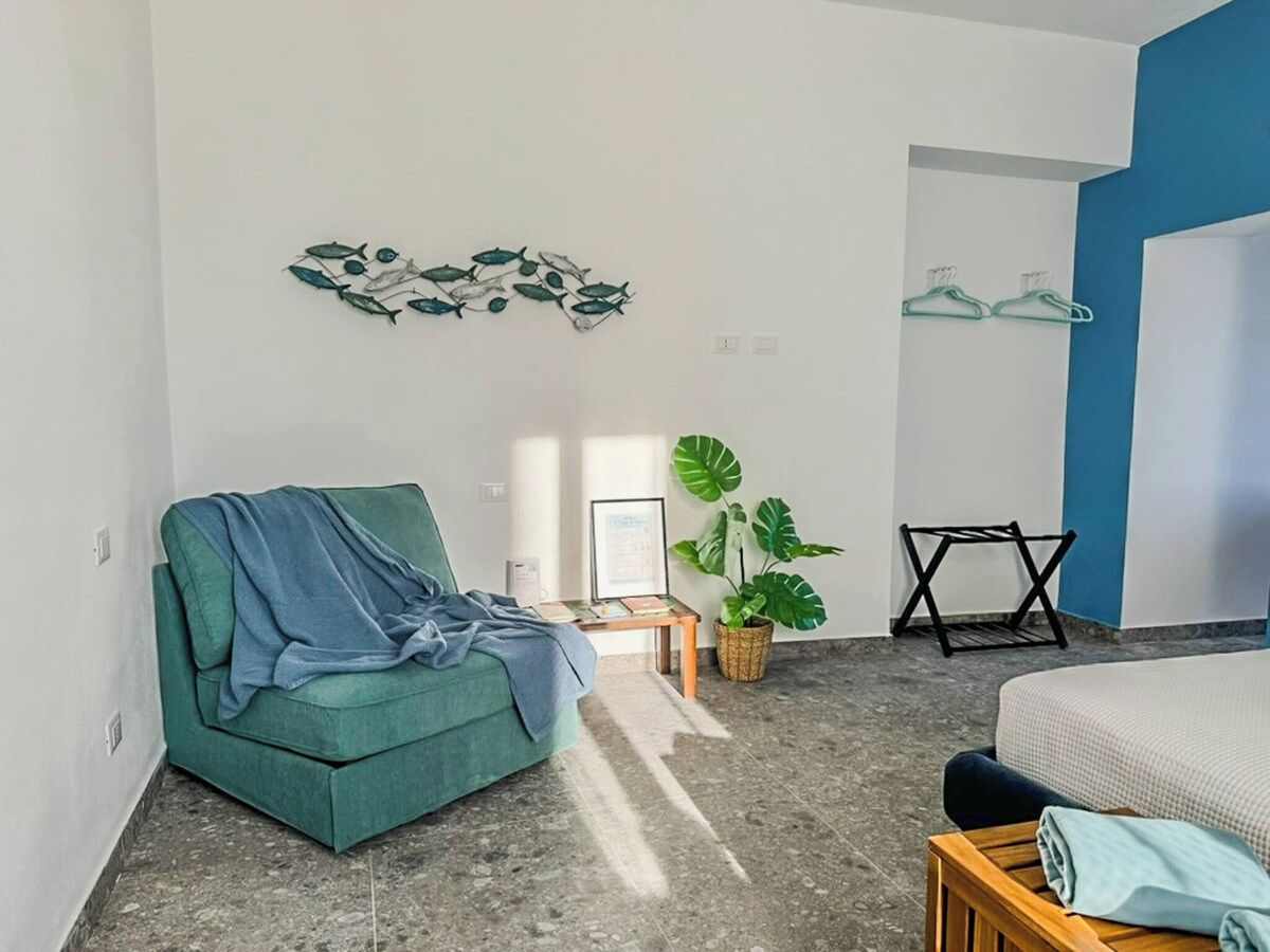 Une pièce avec un canapé vert, un lit, une plante et une œuvre d’art murale.