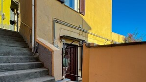 Una escalera estrecha que lleva a una puerta con reja de metal, una pared amarilla y un cielo azul claro.